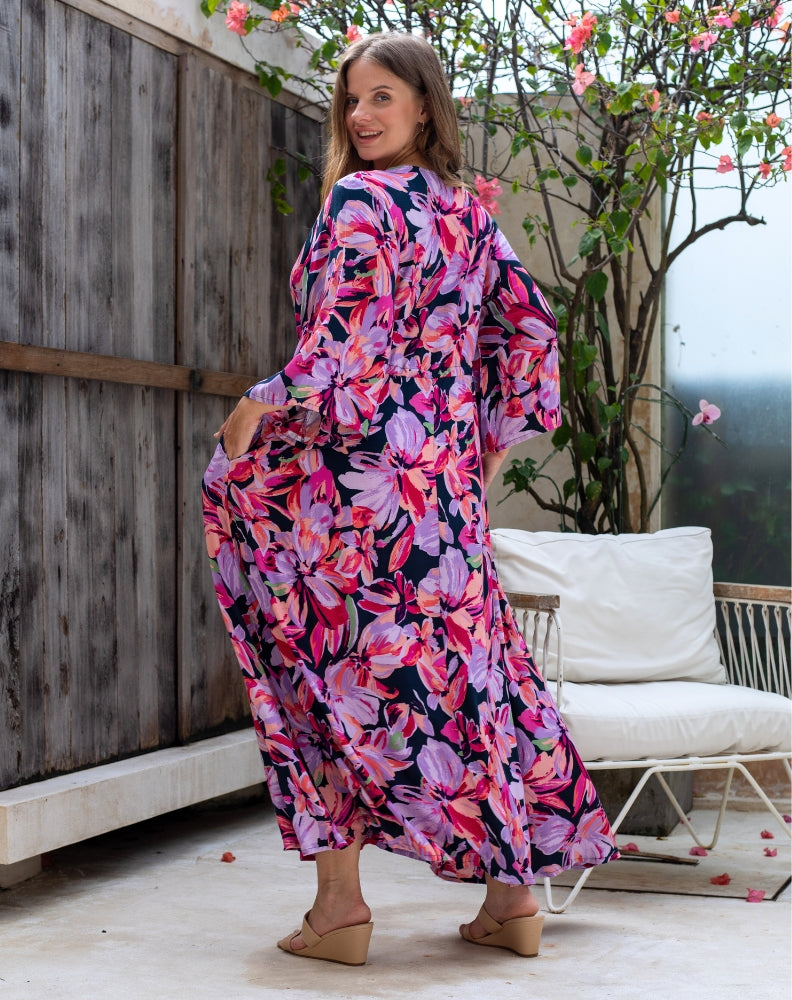 Woman wearing a colorful floral dress standing outdoors near a wooden fence and white chair.