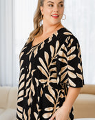 Woman wearing a black dress with beige leaf pattern indoors.