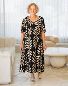 Woman wearing a black dress with beige leaf pattern in a modern living room.