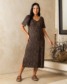 Woman wearing a leopard print dress standing indoors against a neutral wall.