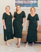 Three women wearing matching green patterned dresses standing together indoors.