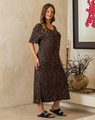 Woman wearing a leopard print dress standing in a room with a decorative wall and plant.