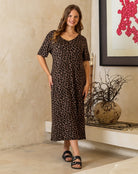Woman wearing a leopard print dress standing in a room with a decorative vase and artwork.