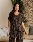 Woman wearing a leopard print outfit standing in a room with a stone wall and couch.