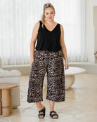 Woman wearing a black sleeveless top and leopard print pants in a living room setting.