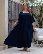 Woman wearing a navy blue dress standing outdoors near a wooden door and plant.