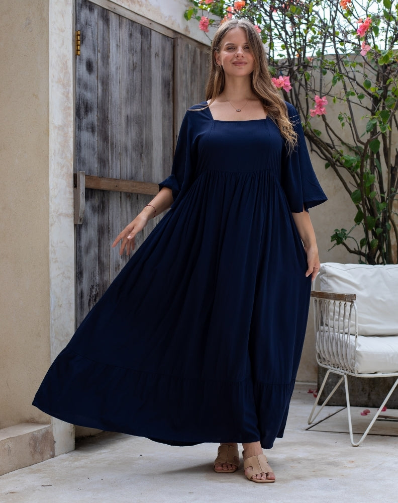 Woman wearing a navy blue dress standing outdoors near a wooden door and plant.