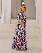 A woman modeling a long-sleeve maxi dress with a colorful floral print, standing in front of a stone staircase.