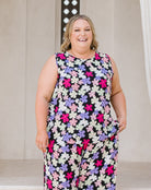 A woman wearing a sleeveless matching set with a colorful floral print, standing in front of a neutral indoor background.