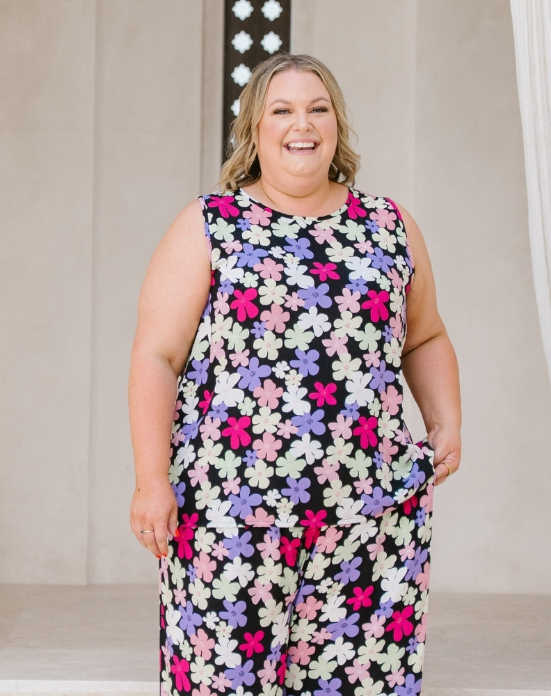 A woman wearing a sleeveless matching set with a colorful floral print, standing in front of a neutral indoor background.