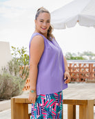 A woman modeling a sleeveless lavender top and a colorful geometric print skirt in an outdoor patio setting.