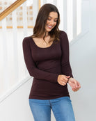 Woman wearing a brown long-sleeve top and blue jeans standing in front of a staircase.