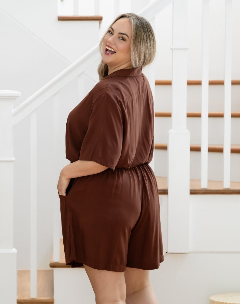 Woman wearing a brown dress standing in front of a staircase.