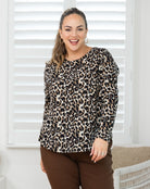 Woman wearing a leopard print top and brown pants in front of white blinds.