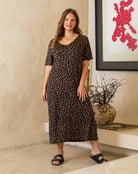 Woman wearing a leopard print dress standing in a room with a decorative plant and abstract art.