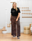 Woman wearing a black t-shirt and leopard print pants standing in a home setting.