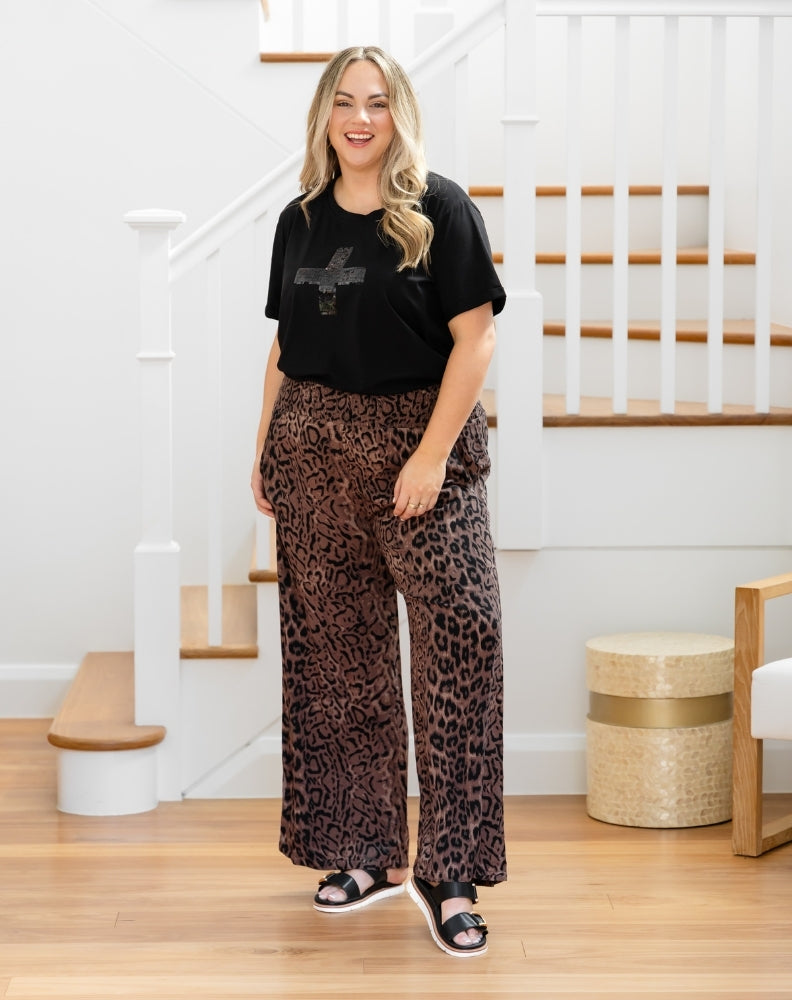 Woman wearing a black t-shirt and leopard print pants standing in a home setting.