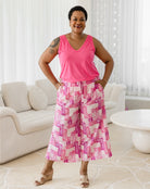 Woman wearing a pink sleeveless top and patterned pants standing in a living room.