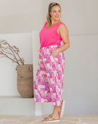Woman wearing a bright pink sleeveless top and patterned pants standing indoors.