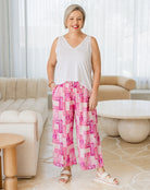Woman wearing a white sleeveless top and pink checkered pants in a living room.