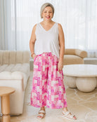 Woman wearing a white sleeveless top and pink checkered pants in a living room.