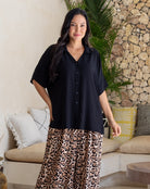 Woman wearing a black shirt and leopard print pants in a living room setting.