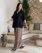 Woman in black top and leopard print pants standing in a modern living room.