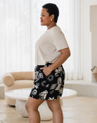 Woman wearing a beige blouse and black patterned shorts in a bright room.