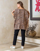 Woman wearing a leopard print top and black pants in a room with a decorative plant and abstract art.