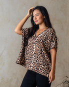 Woman wearing a leopard print top against a beige wall