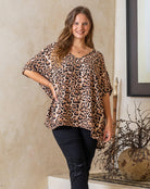 Woman wearing a leopard print top and black pants standing indoors.