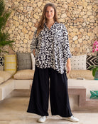 Woman wearing a black and white patterned blouse and black wide-leg pants in a living room setting.
