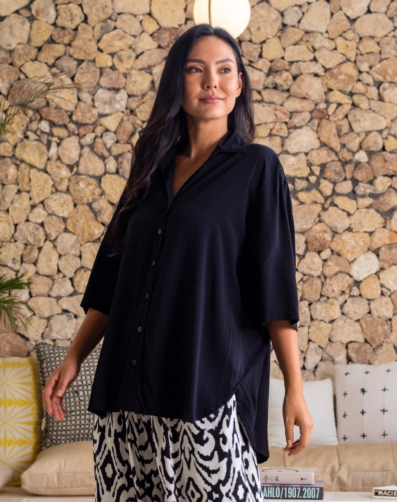 Woman wearing a black shirt and patterned pants standing against a stone wall.