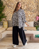 Woman wearing a black and white patterned top and black pants standing in a living room.
