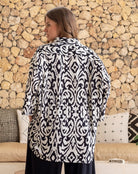 Woman wearing a black and white patterned shirt against a stone wall.