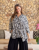 Woman wearing a black and white patterned blouse standing in front of a stone wall.