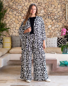 Woman wearing a black and white patterned outfit standing in a living room with stone wall and sofa.