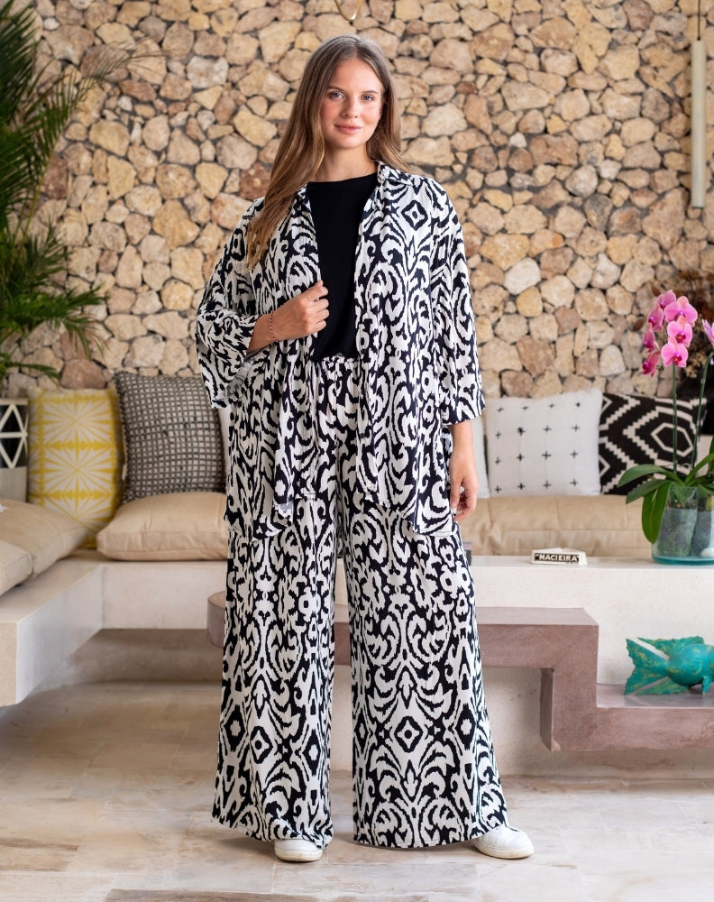 Woman wearing a black and white patterned outfit standing in a living room with stone wall and sofa.