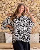 Woman wearing a black and white patterned blouse against a stone wall.