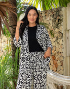 Woman in a black and white patterned outfit standing in a tropical setting with palm trees and stone wall.