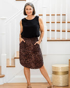 Woman wearing a black sleeveless top and leopard print skirt standing in a home setting.