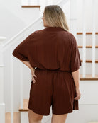 Person wearing a brown romper standing in front of a staircase.