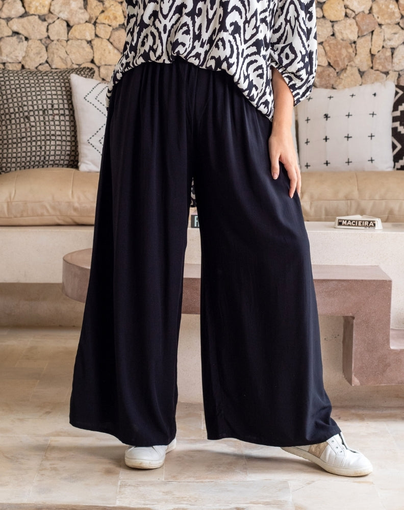 Person wearing black wide-leg pants and a patterned top in a living room setting.