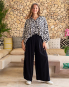 Woman wearing a patterned blouse and black pants standing in a living room.