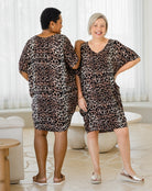 Two women wearing leopard print dresses standing in a room with white curtains.