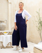 Woman wearing navy blue overalls with a white top in an indoor setting.