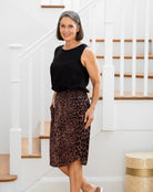 Woman wearing a black sleeveless top and leopard print skirt standing in a home setting.