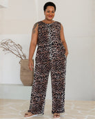 Woman wearing a leopard print jumpsuit standing against a white wall.