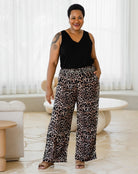 Woman wearing a black sleeveless top and leopard print pants in a room with white curtains.