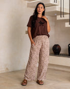 Woman wearing a brown t-shirt with a star design and patterned pants in a modern indoor setting.